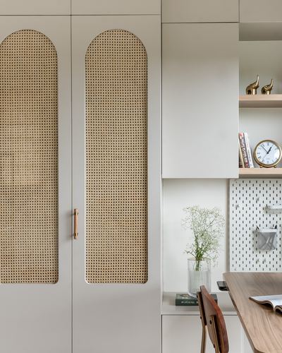Cane-webbed arched wardrobe doors beside a study nook with pegboard, shelf, and wooden desk