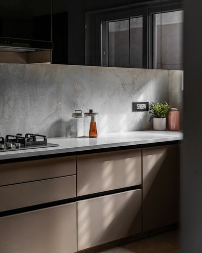 Sunlit kitchen counter with marble-look backsplash, beige cabinetry, and gas hob
