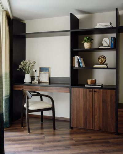 Built-in wooden desk with black shelving unit, decor, and cane-back chair in a study nook