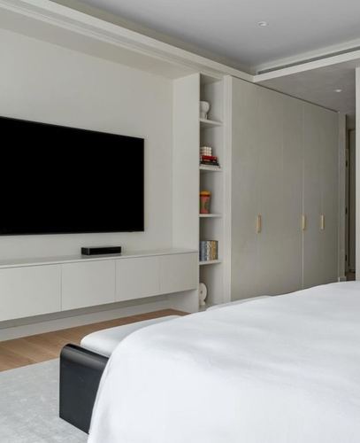 Minimalist bedroom with wall-mounted tv, floating console, open shelving, and beige wardrobe doors