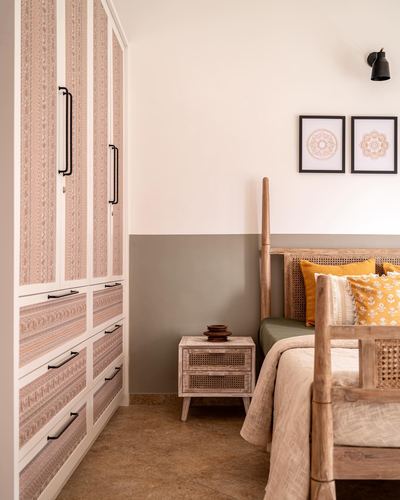 Bedroom corner with cane headboard, mustard cushions, printed wardrobe, and cane nightstand