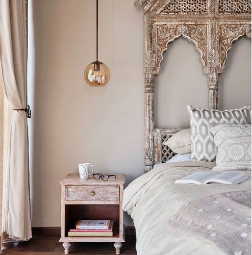 Bedroom with carved distressed arched headboard, amber glass pendant, and wooden bedside table with books