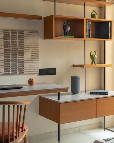 Wall-mounted wooden desk and shelving unit with stone tops against a cream wall, styled with books and figurines