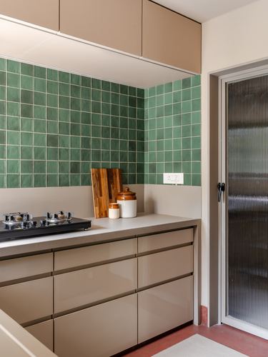 Kitchen corner with green tiled backsplash, beige glossy cabinets, and reeded glass door