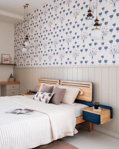 Bed with wood headboard against floral wallpaper, blue floating nightstands, two pendant lights