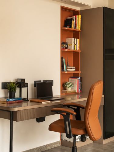 Home study nook with orange bookshelf, wooden desk, laptop and tan leather office chair