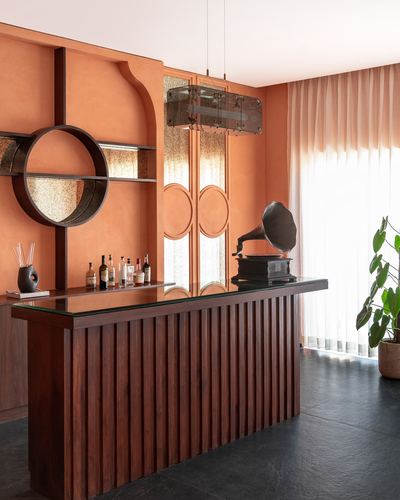 Terracotta-walled home bar with fluted wood counter, round mirror shelf, and vintage gramophone
