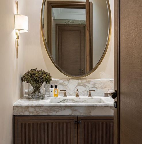 Powder room vanity with marble countertop, oval brass mirror, and fluted wood cabinets