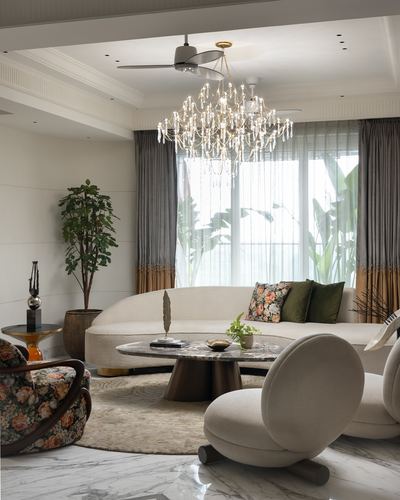 Curved cream sofa and marble round table under crystal chandelier in living room