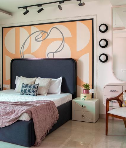 Bedroom with navy upholstered bed against orange abstract mural, pink nightstand and cane chair