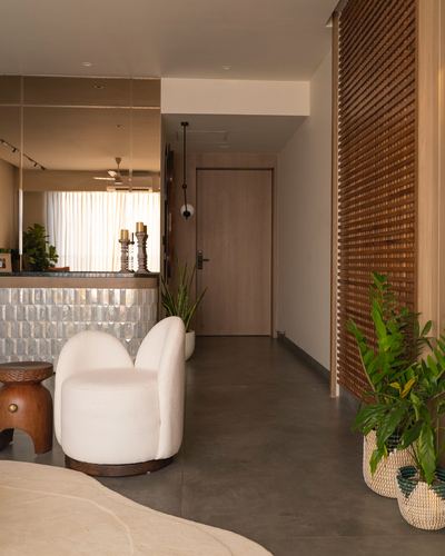 Foyer with wooden slat wall, boucle armchair, wooden stool and plants leading to a wooden door