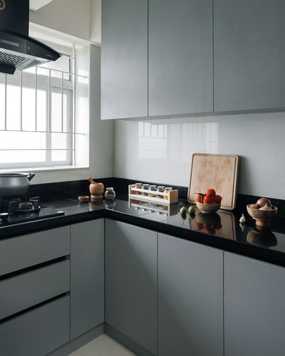 L-shaped modular kitchen with grey cabinets, black countertop, and glass backsplash