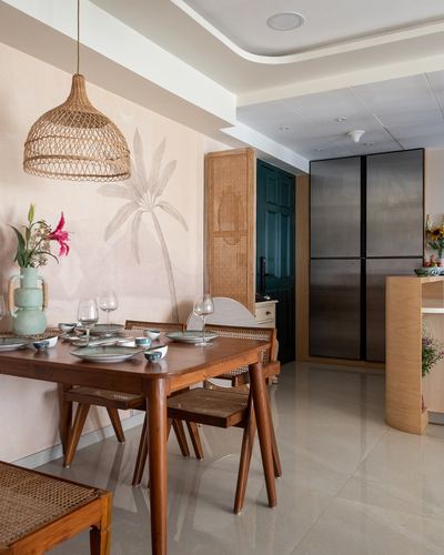 Dining nook with teak table, cane chairs, rattan pendant, and palm mural against pink wall
