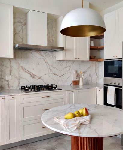 White kitchen with marble backsplash, brass dome pendant, and round marble island table