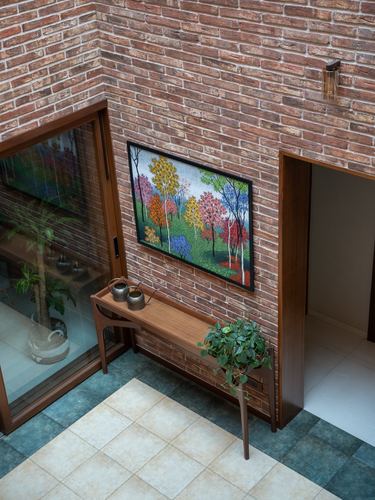 Overhead view of brick-walled entry passage with wooden console, framed forest painting, and potted plant.