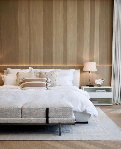 Bedroom with fluted wood headboard wall, white bedding, and taupe bench on herringbone floor