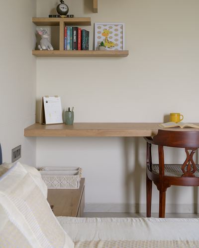 Floating wooden desk in corner nook with cane chair, shelf of books and toys above