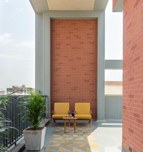 Balcony with exposed brick wall, yellow armchairs, and geometric tiled floor in Vadodara home
