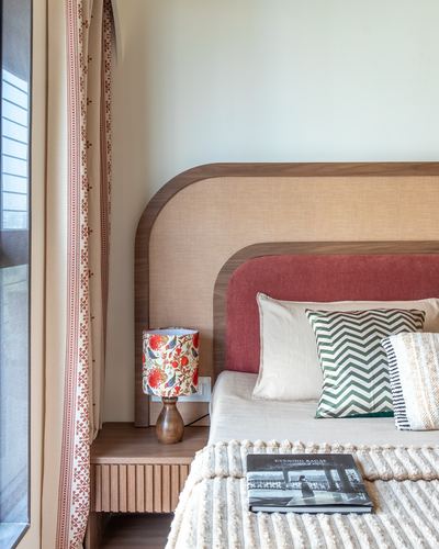 Bedroom corner with curved wooden headboard, terracotta and beige upholstery, patterned lamp and ribbed nightstand