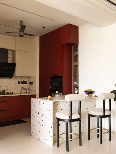 Kitchen with maroon cabinetry, terrazzo island and two cream bar stools with brass legs