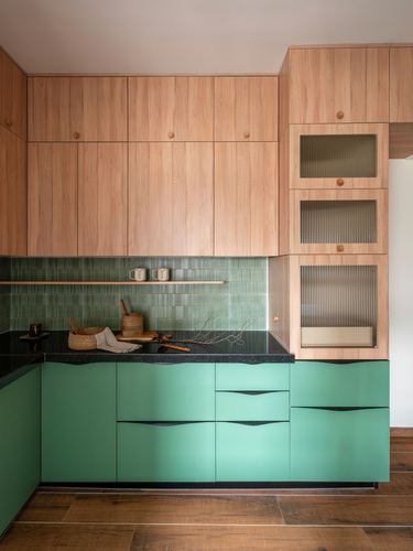 Kitchen with wood upper cabinets, green tile backsplash, black counter, and teal lower cabinetry