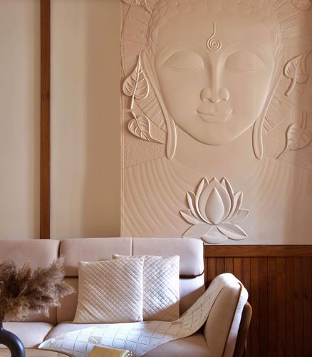 Cream sofa with quilted cushions beneath a sculpted plaster Buddha relief wall