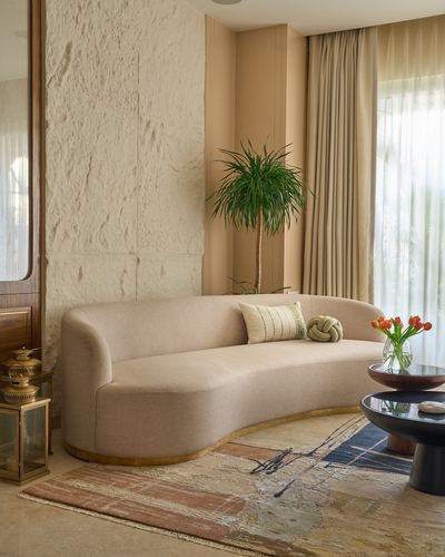 Curved beige sofa against a textured stone wall with a potted plant and round side table