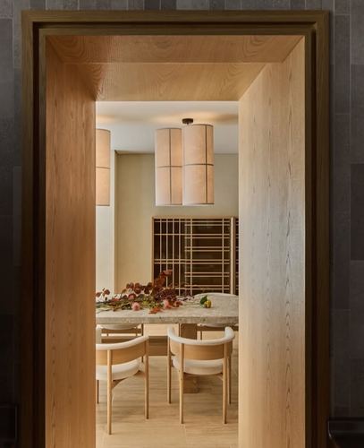 View through a wood-framed doorway into a dining room with cylindrical pendant lights and a stone table