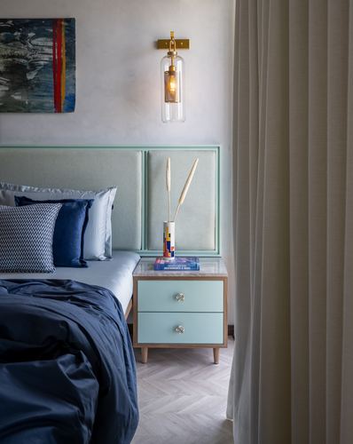 Bedroom corner with mint headboard, navy linens, brass sconce and mint nightstand with marble top