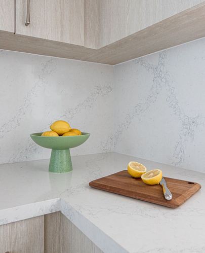 Corner of a kitchen counter with a green pedestal bowl of lemons and a wooden board with cut lemon halves