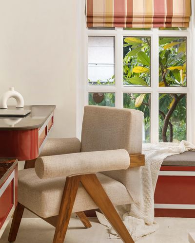 Beige upholstered armchair with wooden bolster arms beside a window seat overlooking greenery