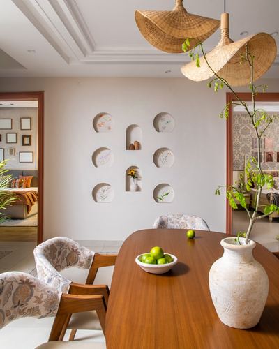 Dining table with ceramic vase under woven pendant lights, wall niches with plates behind