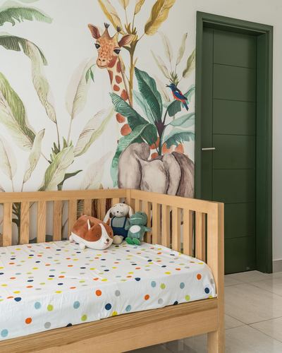 Wooden crib with polka dot sheet against a jungle mural wall, green door beside it