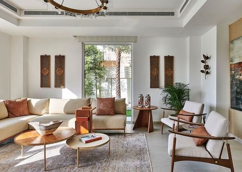Sunlit living room with cream sectional, round wood coffee tables, and carved panels beside a garden-view window