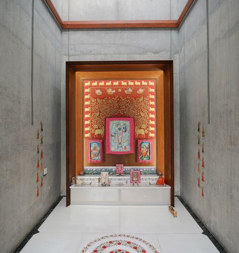 Symmetrical concrete passage leading to a wood-framed pooja niche with religious textiles and marble floor.