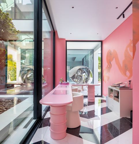 Pink dining nook with sculptural pedestal table, boucle chairs, and herringbone marble floor beside glass courtyard wall
