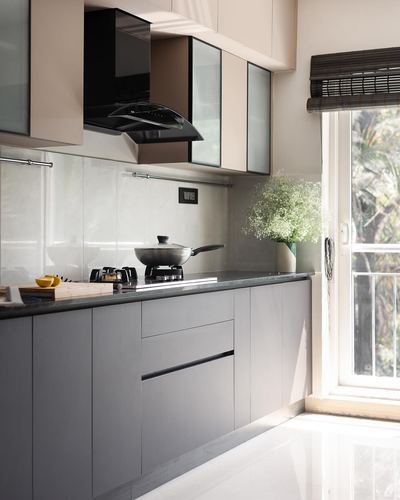 Minimalist grey kitchen counter with black hob, wok, and flowers beside a bright window