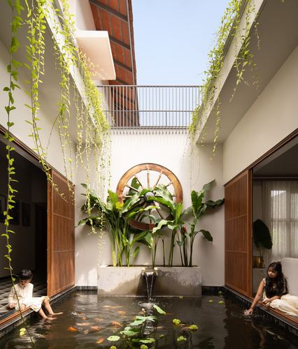 Courtyard koi pond with children, wooden cartwheel sculpture and hanging vines under skylight