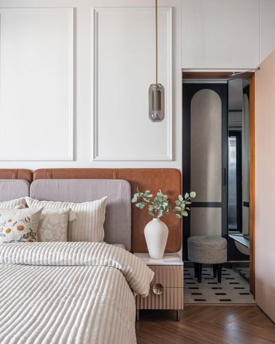 Bedroom with tan leather headboard, pendant light, and glimpse into dressing area with arched mirror niche