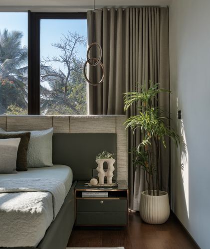 Bedroom corner with textured headboard, dark nightstand, potted plant, and window view of trees