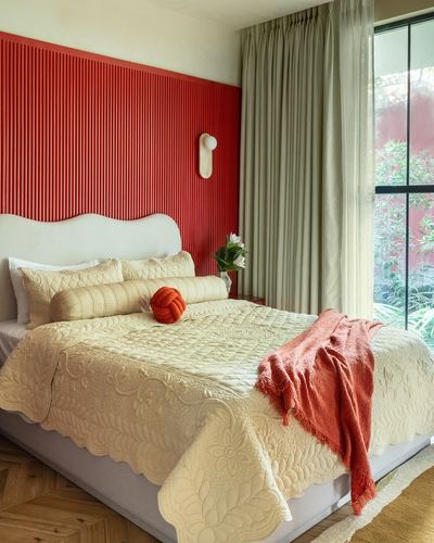 Bedroom with red fluted wall panelling, cream quilted bed, and sage curtains beside a garden-view window