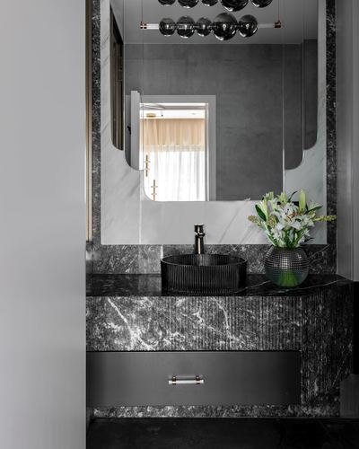 Dark marble bathroom vanity with round vessel sink, arched mirror and flowers
