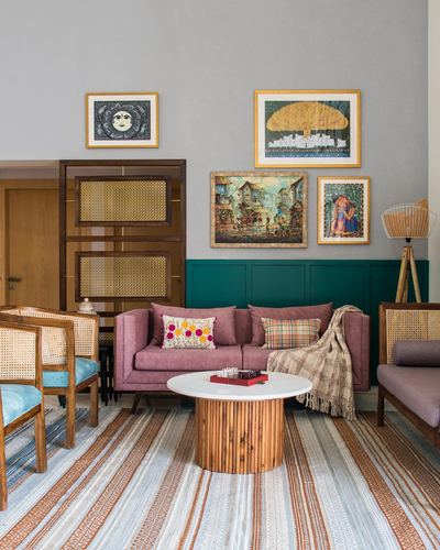 Living room with mauve sofa, teal wainscoting, cane furniture, and a gallery of framed art