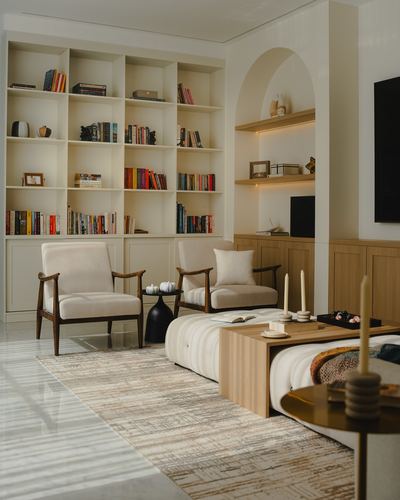 Living room with cream bookshelf, arched niche, two wood-framed armchairs, and low wooden coffee table