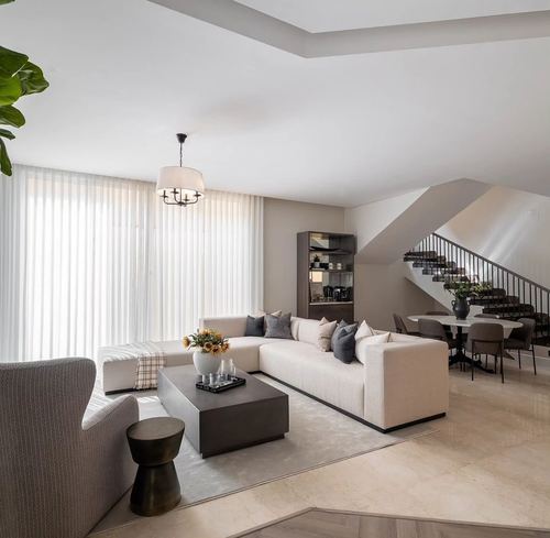 Neutral toned living room with sectional sofa, dark coffee table and staircase in background