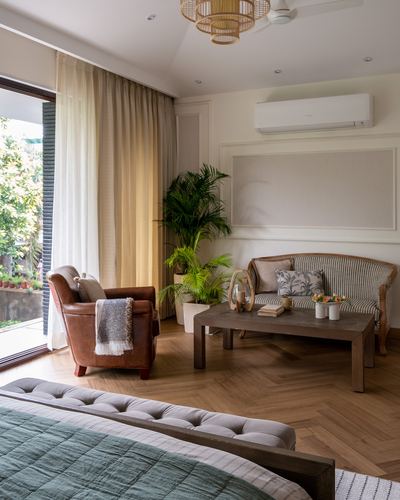 Bedroom sitting area with leather armchair, cane settee and herringbone wood floor beside glass door