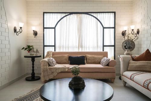 Living room with blush sofa beneath an arched black-framed window and white brick walls
