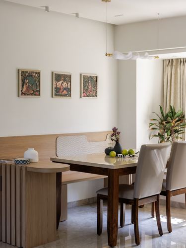 Dining nook with wood bench, cane-backed panel, marble table, upholstered chairs and framed miniature paintings