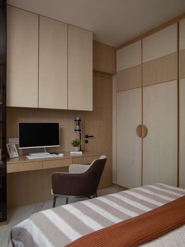 Wood-panelled bedroom study nook with desk, monitor, brown chair, and fluted wardrobe beside a bed