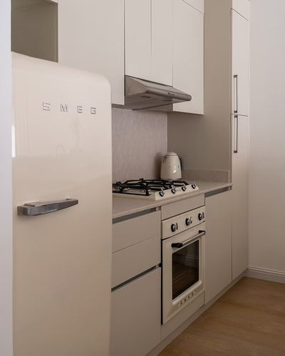 Cream Smeg fridge, cooktop, and oven built into a minimalist cream kitchen with stone countertop